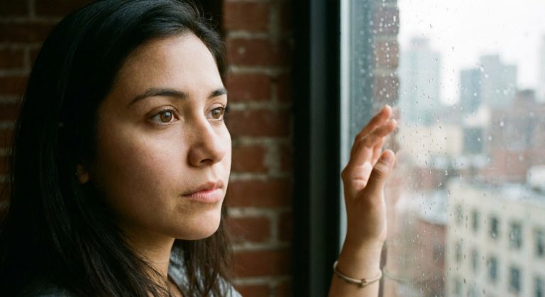 Close up portrait of a young woman looking out a window with a serious expression.